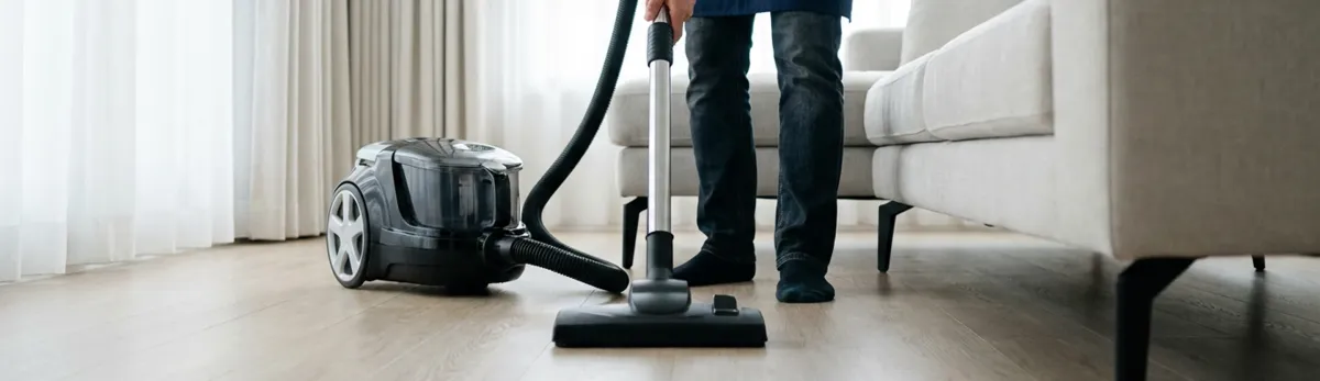 Professional house cleaner vacuuming a living room floor with a canister vacuum cleaner, West Palm Beach, FL.