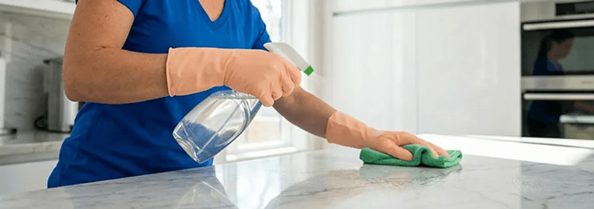 Maid service worker spraying and wiping a kitchen countertop with a microfiber cloth for sanitizing, West Palm Beach, FL.